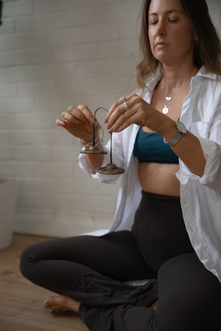 Kim Yates seated in meditation, holding tingsha chimes