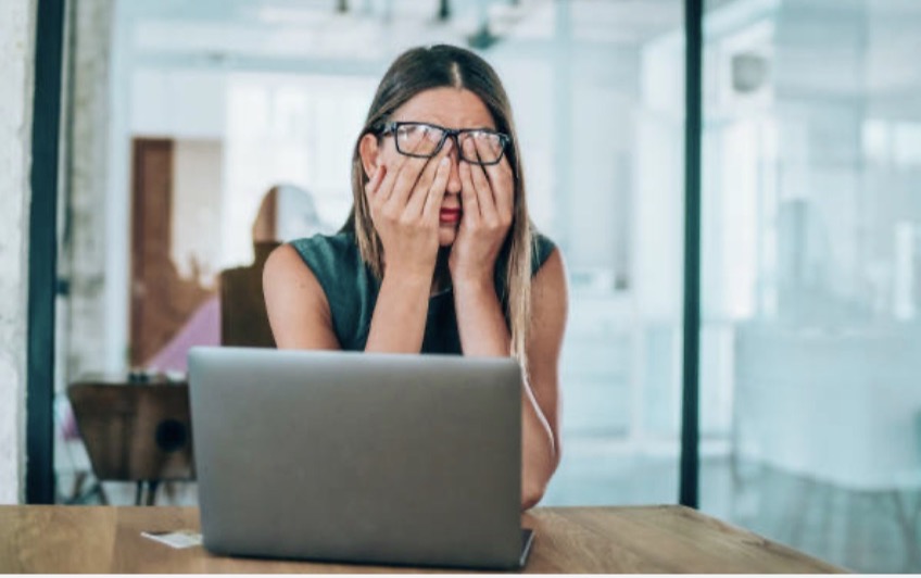 A stressed woman at her desk with her head in her hands in front of a laptop